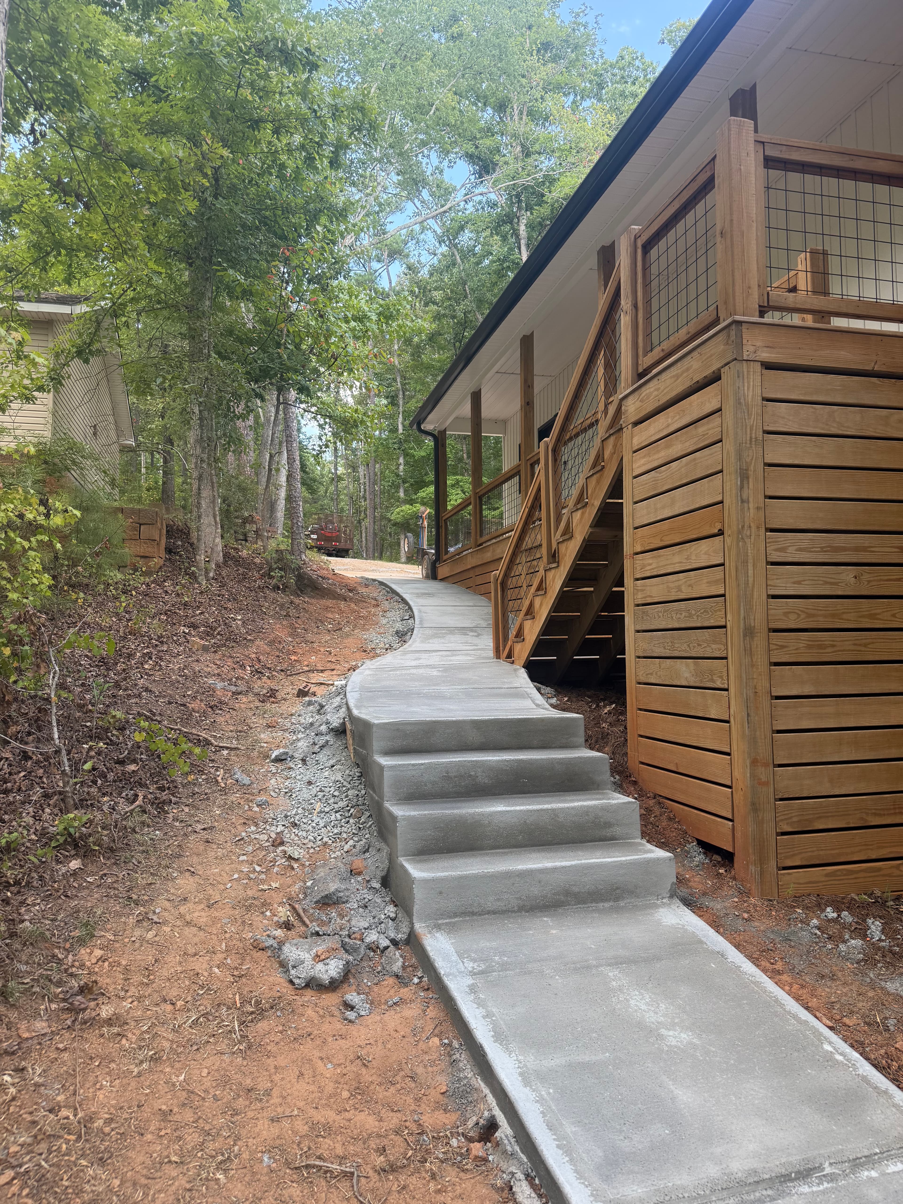 New concrete walkway and stairs wind up a wooded hill next to a wooden deck.