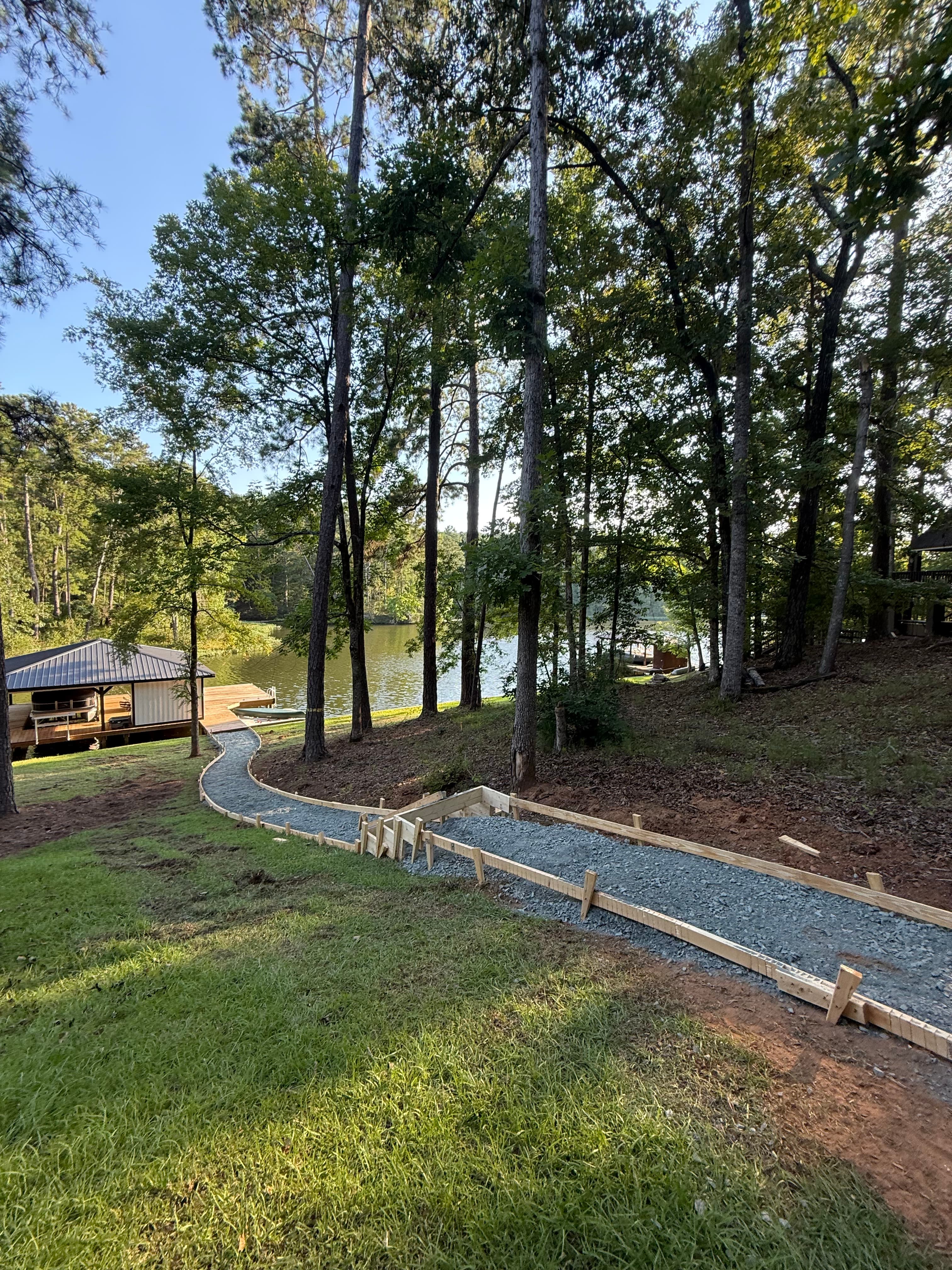 Wooden-framed gravel path winds down a grassy hill toward a lake and boathouse.
